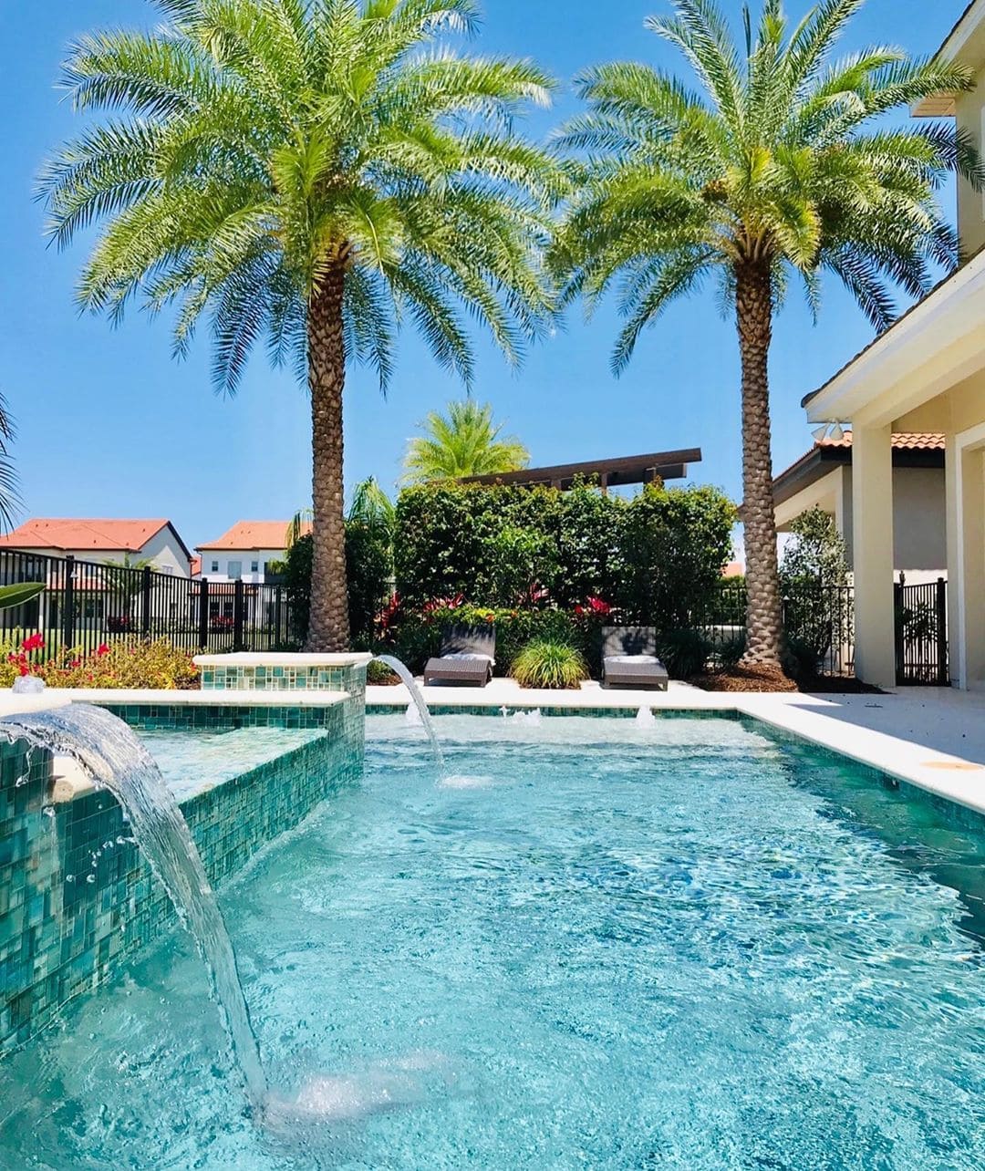 backyard pool with spa and small waterfalls and palm trees