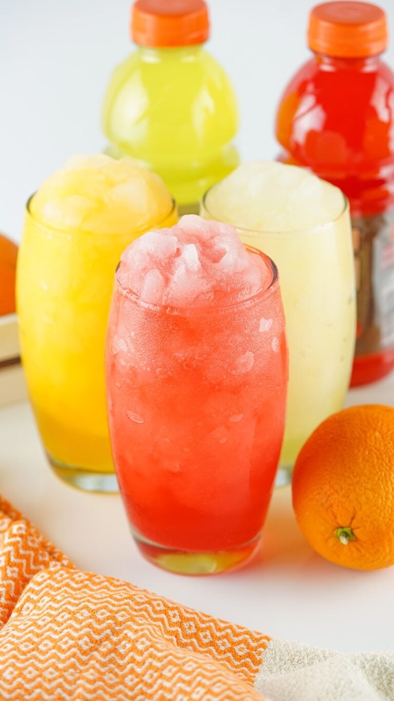 Three colorful Gatorade slushies with an orange and bottles in the background.