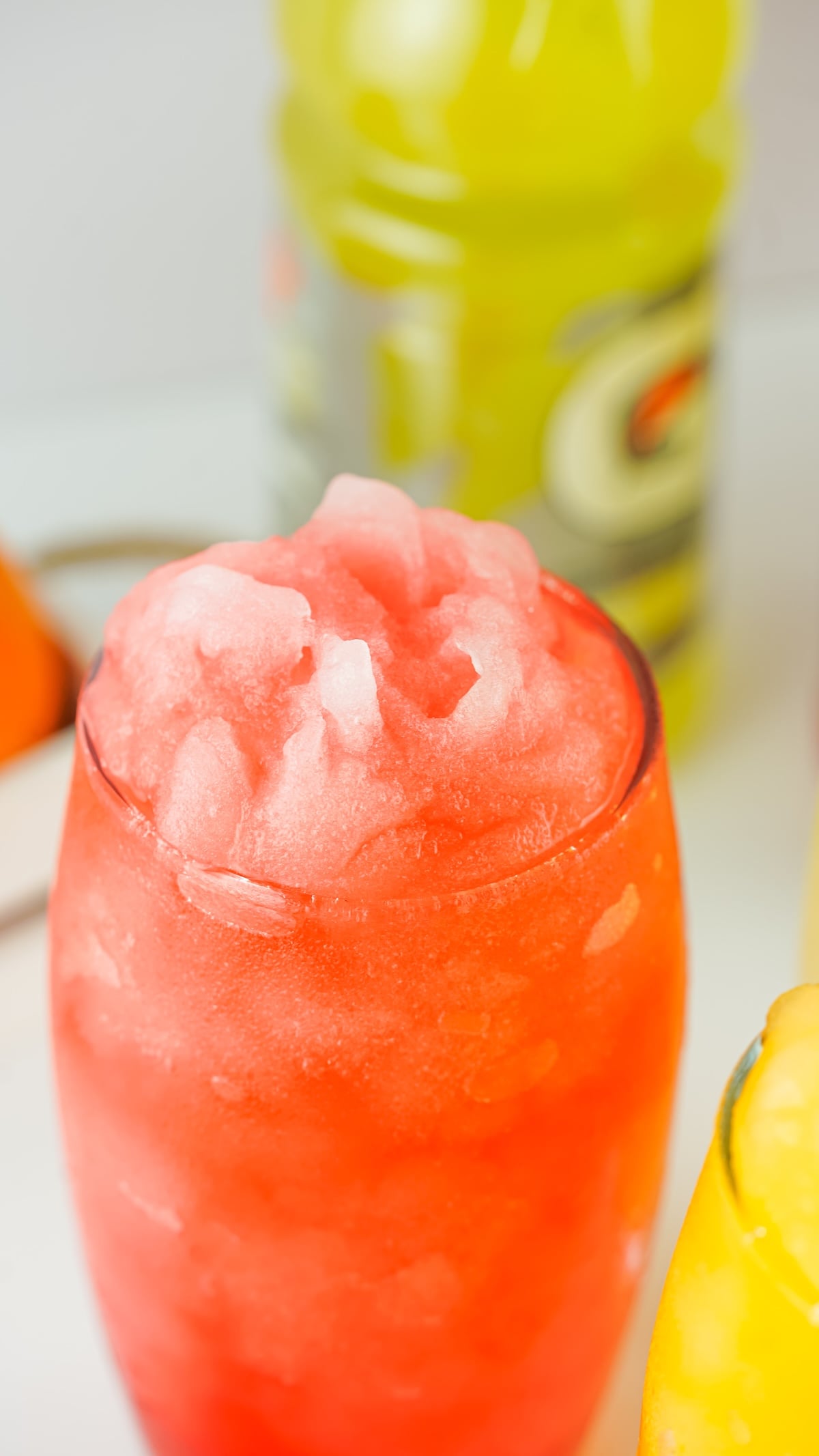 Bright red-orange Gatorade slushie in focus with a yellow drink and bottle blurred in the background.